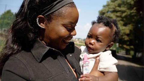 A mother holds her baby and smiles at her.