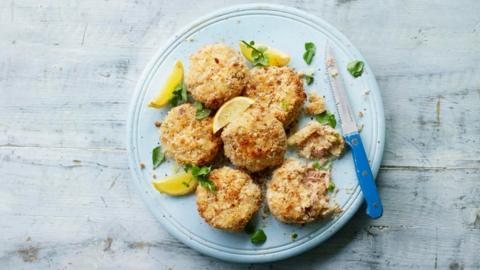 Fish cakes on a blue plate on a white washed surface with a knife and lemon wedges