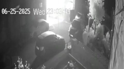 A black and white still from a security camera shows a terraced house engulfed in a ball of bright light moments before it exploded.
