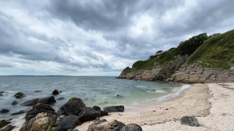 Cloudy sky over a beach surrounded by rocks and headland at Carsluith, Dumfries and Galloway