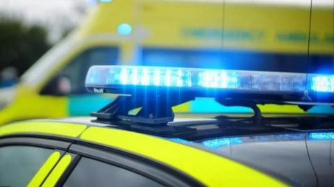 Generic shop of the top of a police car's lights. There is an ambulance in the background which is out of focus. 