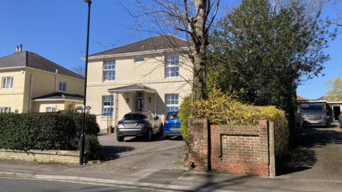 The front of a cream coloured building with two cars parked outside