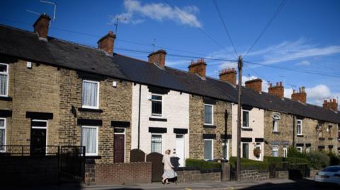 A woman walks down a row of traditional terraced houses in Barnsley