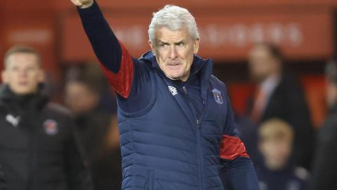 Mark Hughes with his right arm raised and his index finger pointed in the direction of Carlisle fans