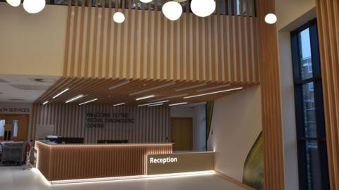 The wooded interior of the centre's reception. A bright reception desk is in the middle of the shot, with wood panelling stretching to the ceiling and the floor above.