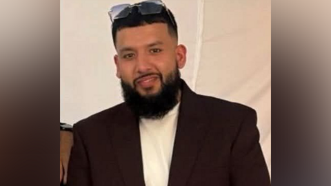 A man with a black beard and glasses on top of his head is looking at the camera.