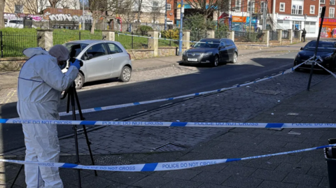 Police forensic teams photograph a street within a police tape cordon in Bristol