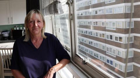 Image of Jackie stood by her window in her flat