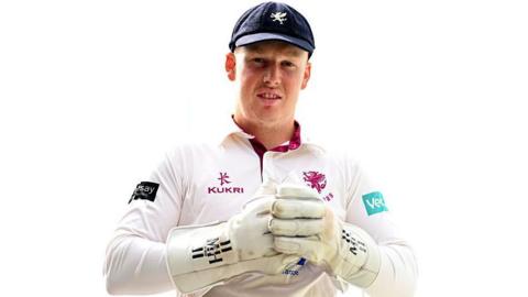 James Lew, dressed in Somerset's white cricket kit and wearing white wicketkeeper gloves and a blue cap