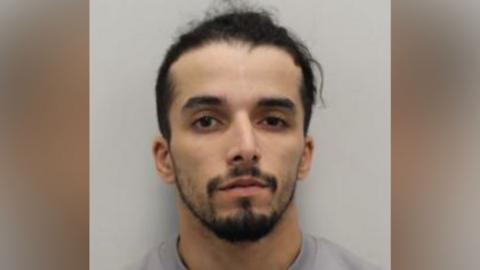 Brahim Kaddour-Cherif wears a grey sweater. He has a beard and moustache