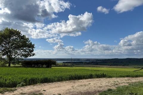A bright countryside landscape with a green fields, and a blue sky filled with scattered fluffy clouds in Cumnor, Oxfordshire