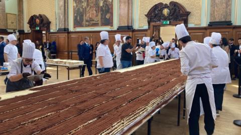 Chefs work on a long tiramisu on a table