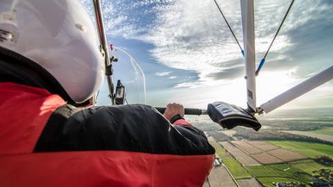 A view from inside a microlight aircraft over the pilot's shoulder to fields below