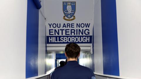 An image of a player walking through a tunnel with a sign above him saying 'You are now entering Hillsborough' with an image of the Sheffield Wednesday club badge