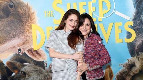 Actors Molly Gordon and Julia Louis-Dreyfus attend "The Sheep Detectives" New York Premiere. They both star in the film and are standing in front of a large poster that features pictures of sheep and the name of the film.