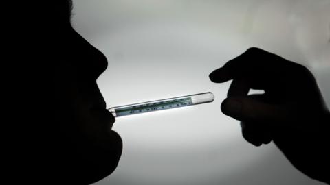 Thermometer in mouth of a patient (in silhouette).