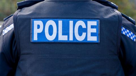 UK police officer close-up of the back of a stab vest with the Police logo prominent.