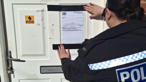 A police officer is sticking an order which has been typed onto a piece of paper, on the white front door of the Wisbech property. 