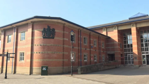 The court building is pictured with the entrance to the right. It is a red and brown brick building.