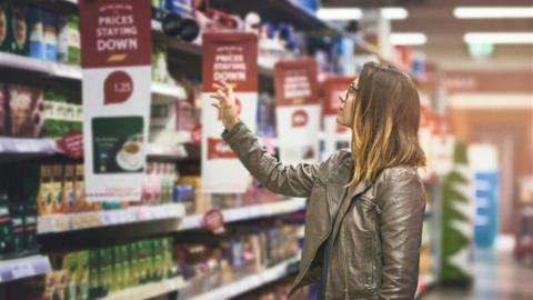 Woman wearing brown leather jacket reaching up to a shelf in a supermarket