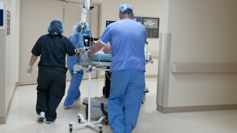 Shows a hospital ward with medical staff wheeling a patient on a trolley