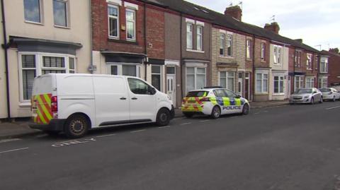 View of a police car and a white van parked on a street of two-storey houses