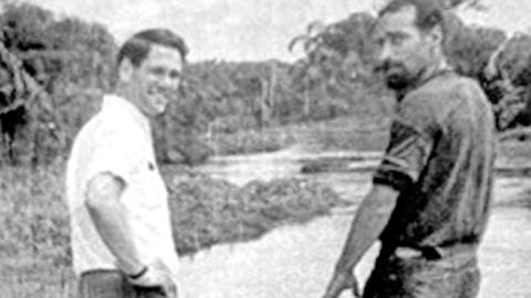 A black and white photo of two men standing on a bridge