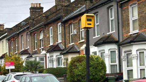 Fake yellow speed camera in a planter next to a row of houses