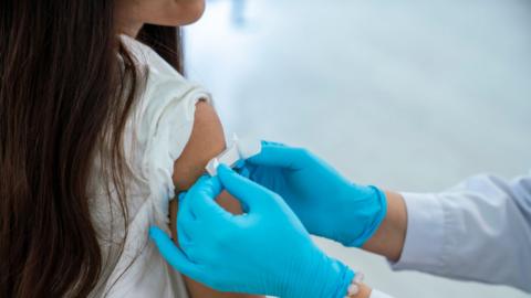 A plaster is applied by a medical worker with blue gloves to the upper arm of a young girl after vaccination