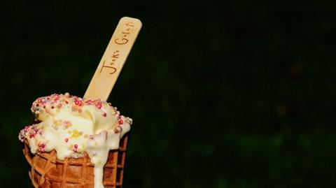 Ice cream, dotted with multi-coloured 100s and 1,000s, spilling over a waffle cone. A wooden spoon branded "Jack's Gelato" is sticking out of the top.