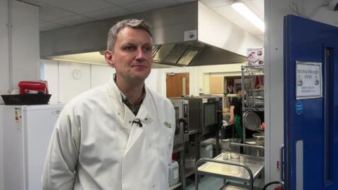 Adam Curtis, of Dolce School Catering in Manchester, stands in a kitchen wearing a white overall