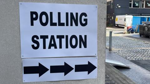 A black and white Polling Station sign stuck to a grey concrete wall
