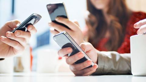 A group of three people look at their phones