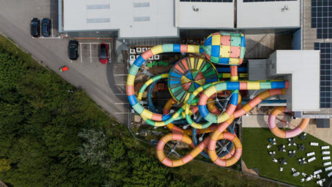 An aerial view of the Waterworld water park, showing multicolour slides twisting to the ground. The image also shows a car park and several trees next to the building.
