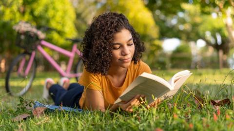 a girl lying in the grass, reading a book