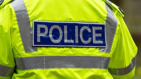 A close-up of the back of a police officer's high-vis yellow jacket. It has the word 'police' across the back. 