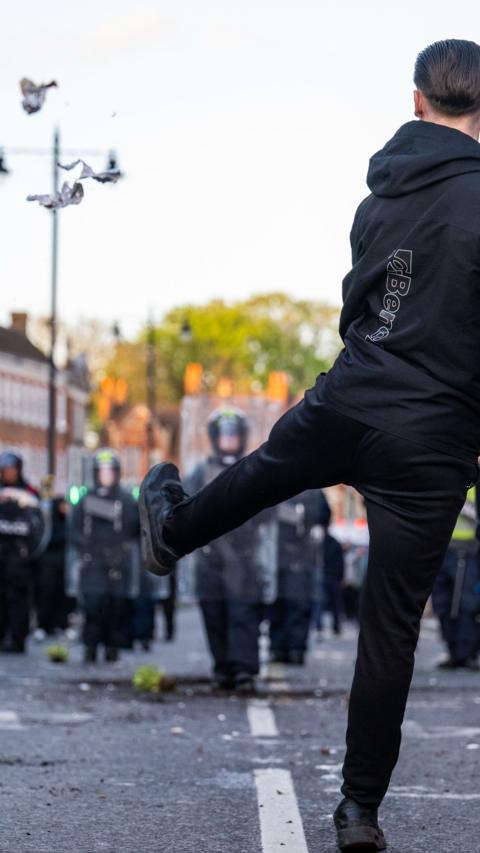 A man facing away from the camera, facing towards riot police