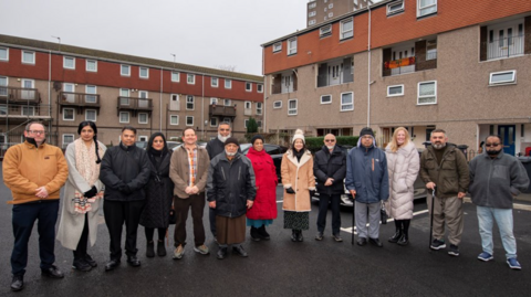 A group of 14 people standing on freshly laid parking spaces 