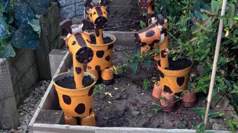 Orange and black giraffes made out of plant pots placed in garden.