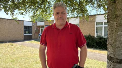 Headteacher Brian Morton stands outside the front of his school under a tree