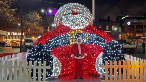 The UK's largest light-up Santa installation behind a man who is dressed up as Santa Claus himself