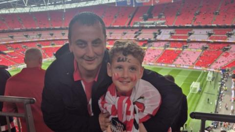 Brian Soulsby and his son Ben are standing in the South Stand at Wembley Stadium ahead of Sunderland's match with Sheffield United. The duo are both dressed in red and white Sunderland shirts. 