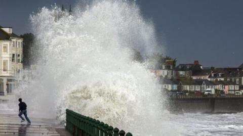 A boy runs from sea spray after a wave crashes into the shore.