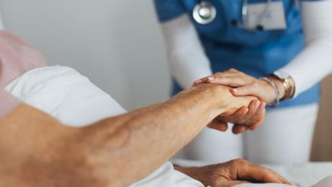 An NHS worker holds the hand of a patient