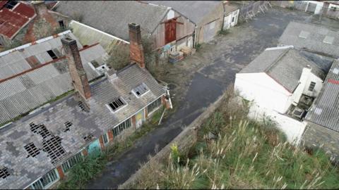 Leale's Yard from the air. A collection of grey derelict buildings with green pampas grass growing in the bottom right corner.