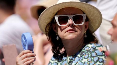  A spectator holds a handheld fan as they watch on day eleven of The Championships Wimbledon 2025