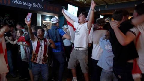 A large group of England football fans gathered in The Hyde Dendy pub in Paignton to watch the game against Mexico. They are celebrating a goal jumping up in the air.