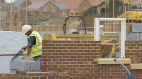 New build houses on a development under construction. A worker is using a saw.