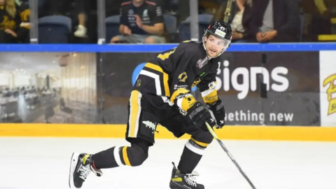 Adam Johnson in a black, yellow and white kit, skating.