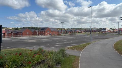 An empty car park with houses behind it.